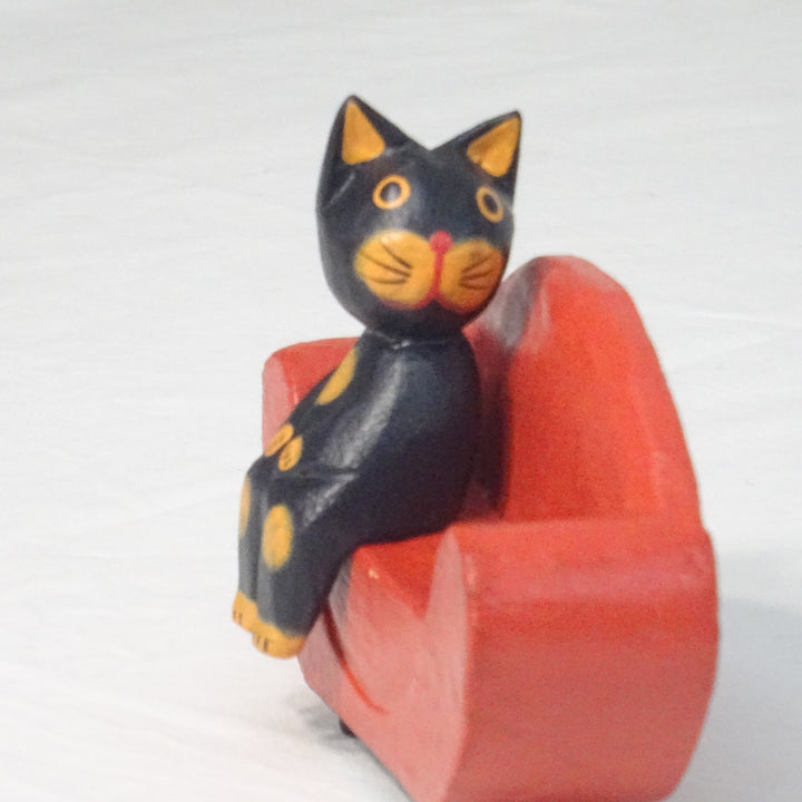 Black canoodling cat sitting on a red sofa